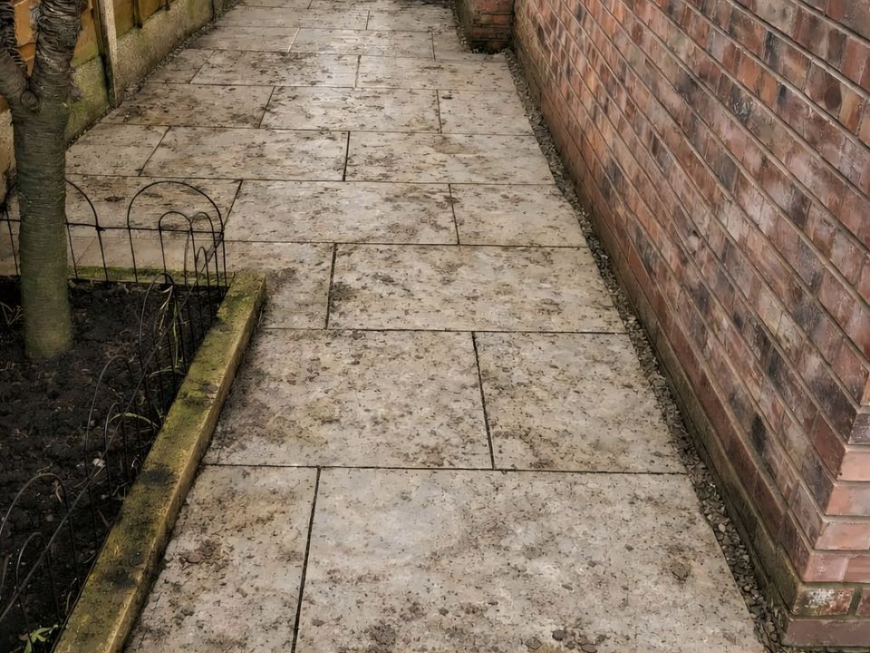Before: Paved side path beside a brick wall, the slabs stained and grubby before jet washing