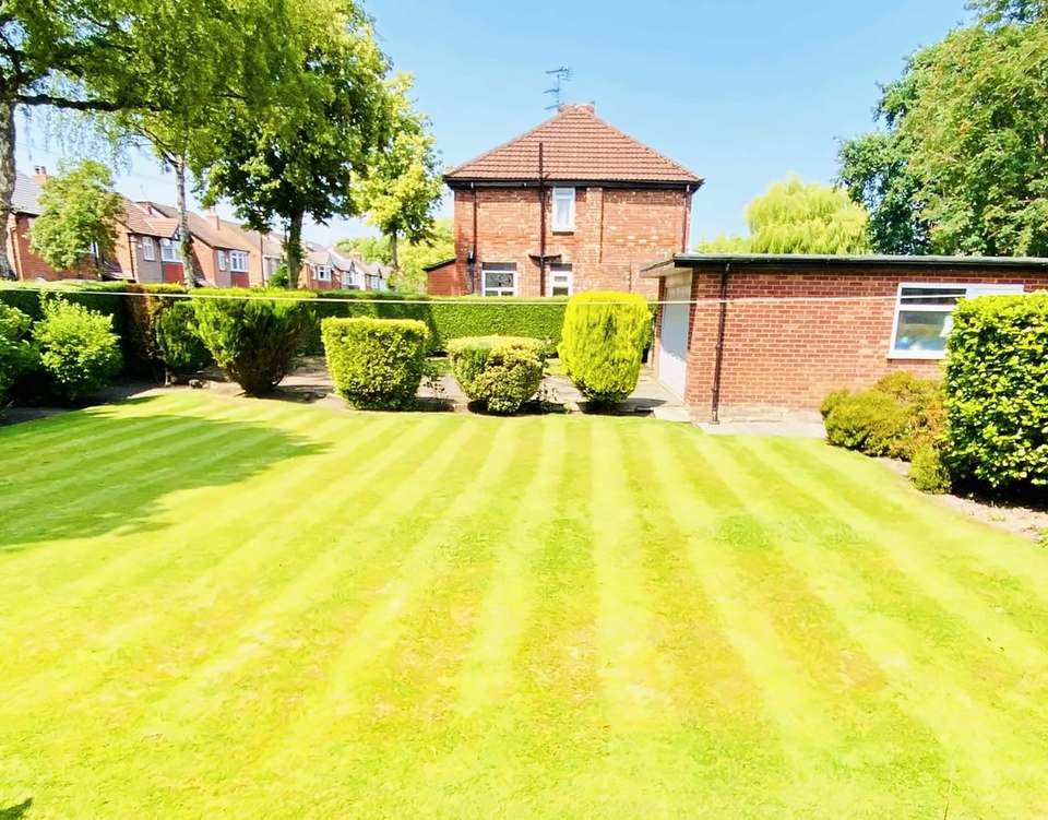 Striped lawn in front of clipped shrubs and a hedge, with a brick garage and house behind